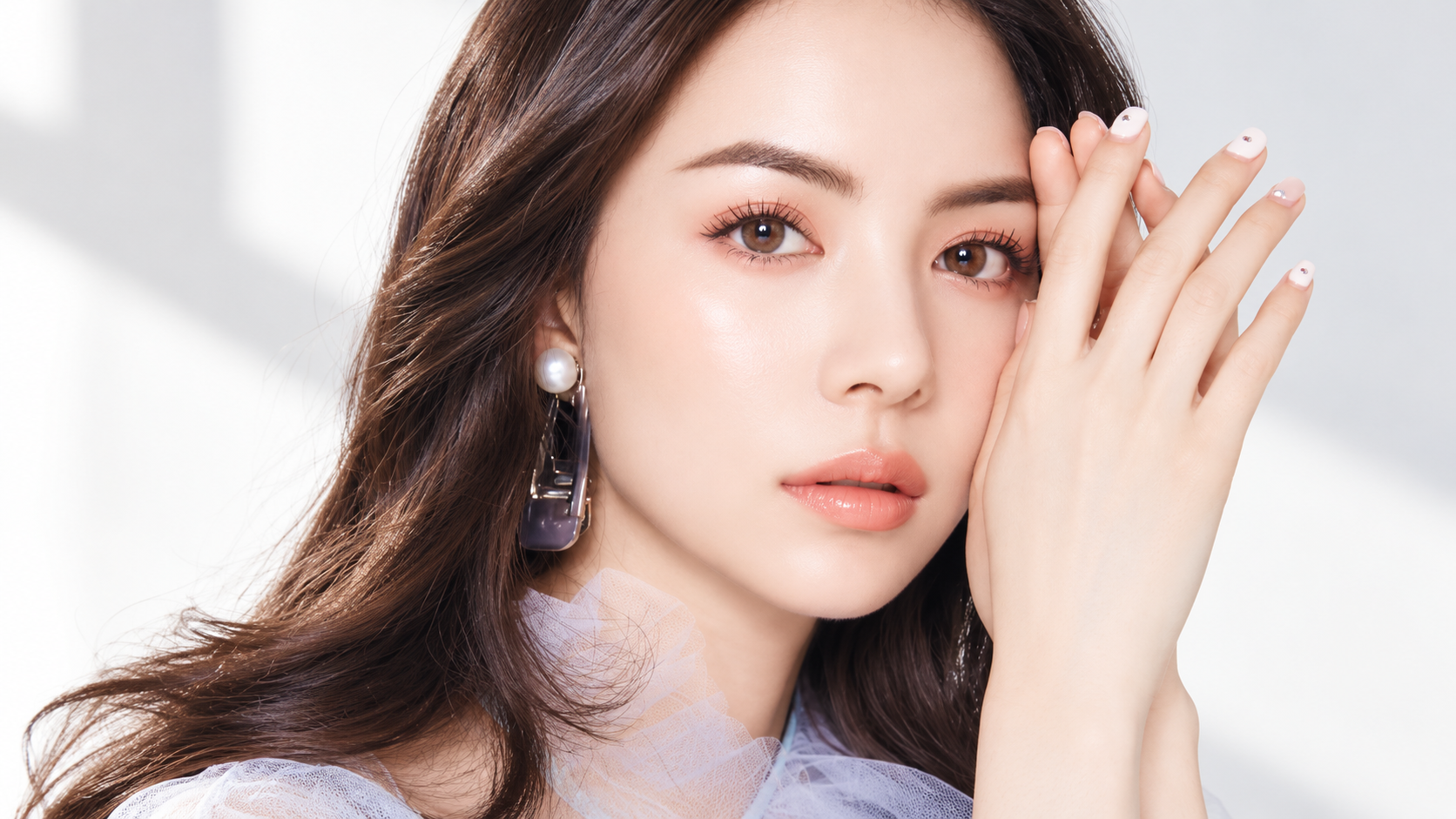 Model with pearl earrings holding her hands beside her eye to illustrate firm skin around the eyes
