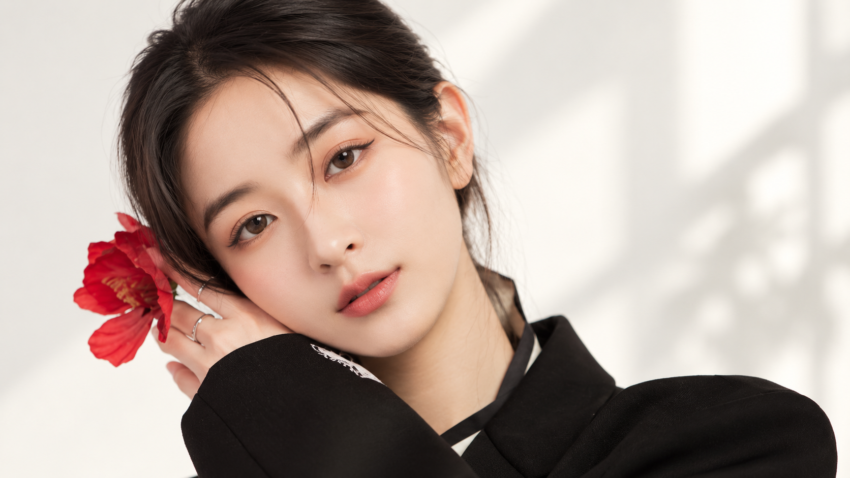 Model in a black jacket holding a red flower beside her face to illustrate clear, flawless skin