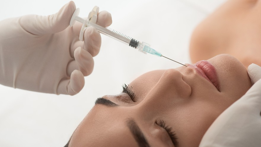 Profesional sanitario administrando una inyección en el labio superior de una paciente.