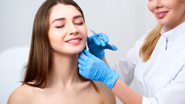 Practitioner administering a facial injection near a woman's cheek.