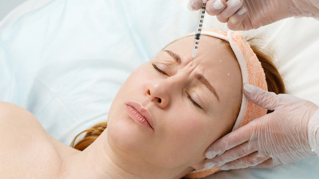 Practitioner administering a facial injection near a woman's forehead.