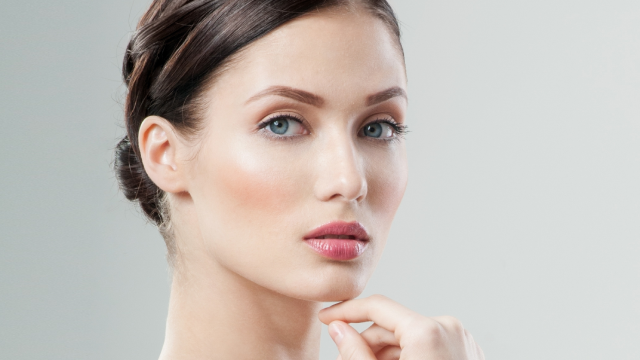 Model with her fingers under her chin against a gray backdrop to illustrate a defined jawline