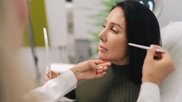 Practitioner examining a woman's face during a consultation.