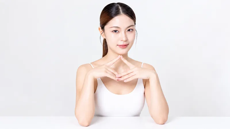 Woman posing with her hands beneath her chin against a white background.
