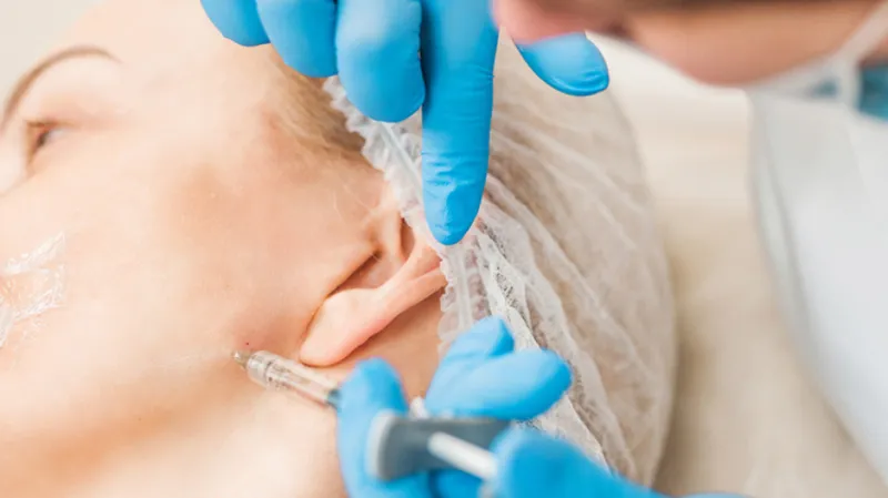 Practitioner administering an injection near a woman’s ear.