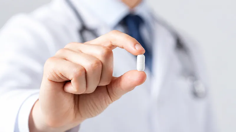 Medical professional holding a white capsule between two fingers.