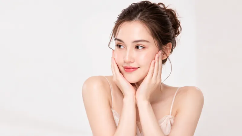 Woman touching both cheeks while looking to the side against a white background.