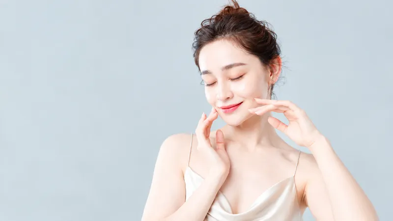 Woman touching her cheeks with eyes closed against a light background.