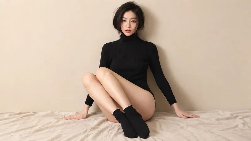Woman in a black bodysuit seated against a beige wall.