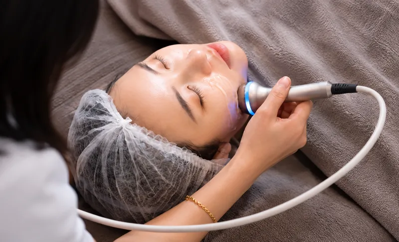 Practitioner using a handheld device on a woman’s lower face.