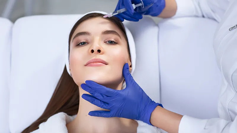 Practitioner holding a syringe near a woman’s forehead.