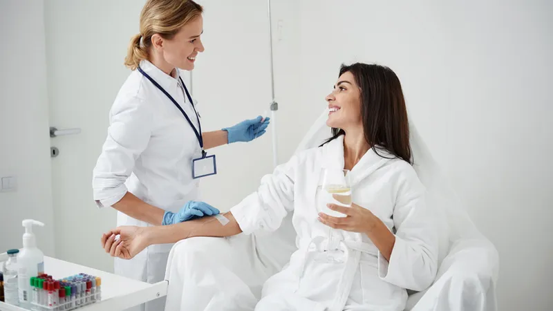 Practitioner attending a seated woman with an IV line in her arm.
