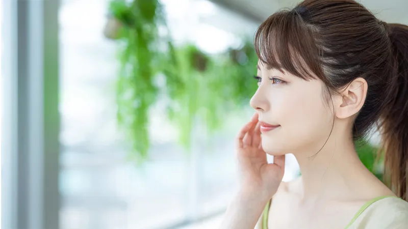 Woman touching her cheek while looking to the side.