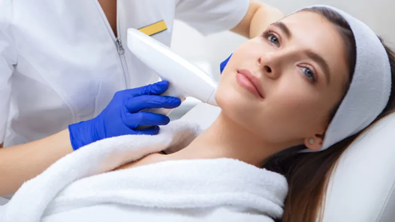 Practitioner using a handheld device on a woman’s jawline.