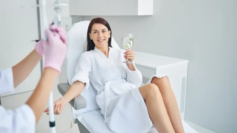 Woman receiving an IV infusion while holding a glass of water.