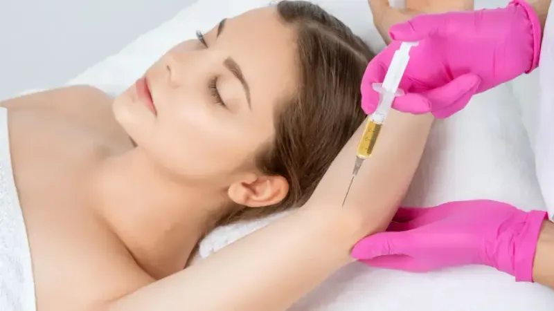 Practitioner holding a syringe near a woman’s upper arm.