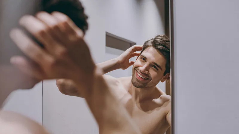 Shirtless man looking at his reflection in a mirror.