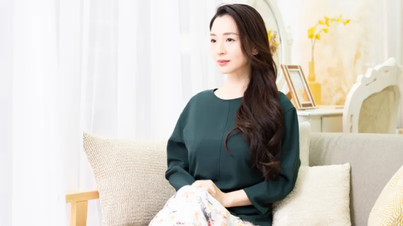 Woman with long dark hair seated on a sofa.