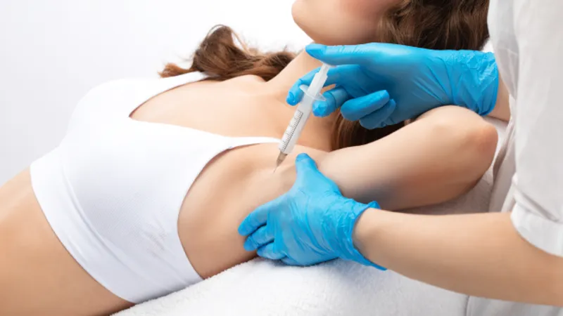 Practitioner holding a syringe near a woman’s underarm.