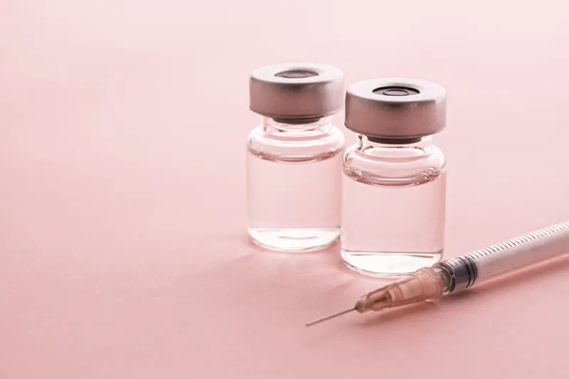 Syringe beside two unlabeled medical vials on a pink background.