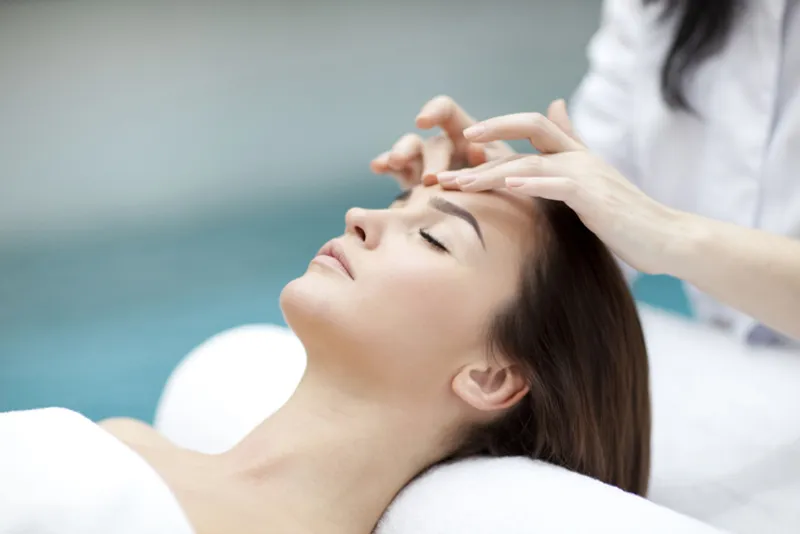 Practitioner massaging a woman’s forehead during facial treatment.
