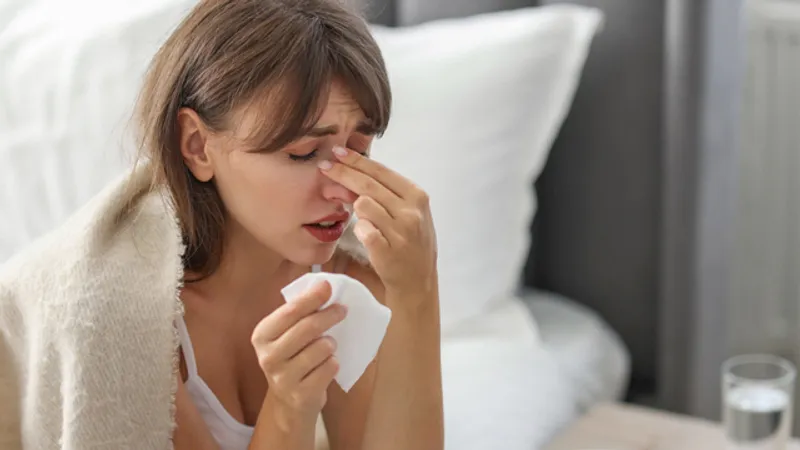 Woman holding a tissue and touching the bridge of her nose.