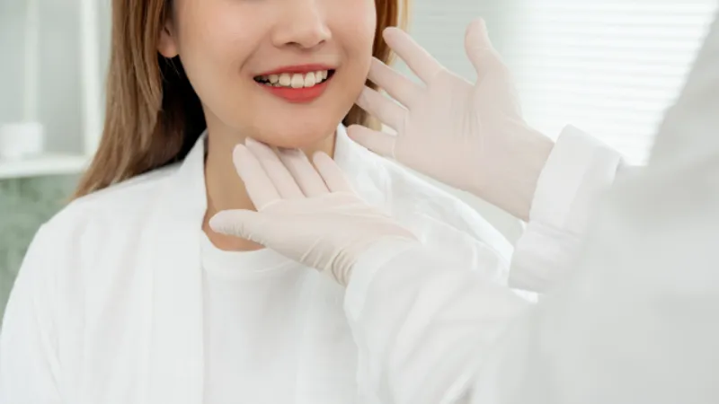 Practitioner examining a woman’s jawline while wearing medical gloves.