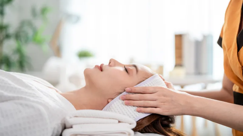 Practitioner placing hands near a woman’s head during a facial treatment.