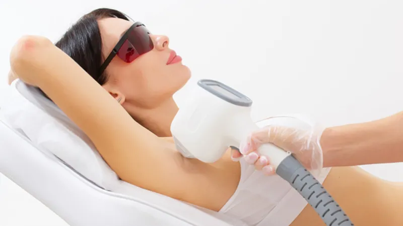 Practitioner applying a handheld device to a woman’s underarm.