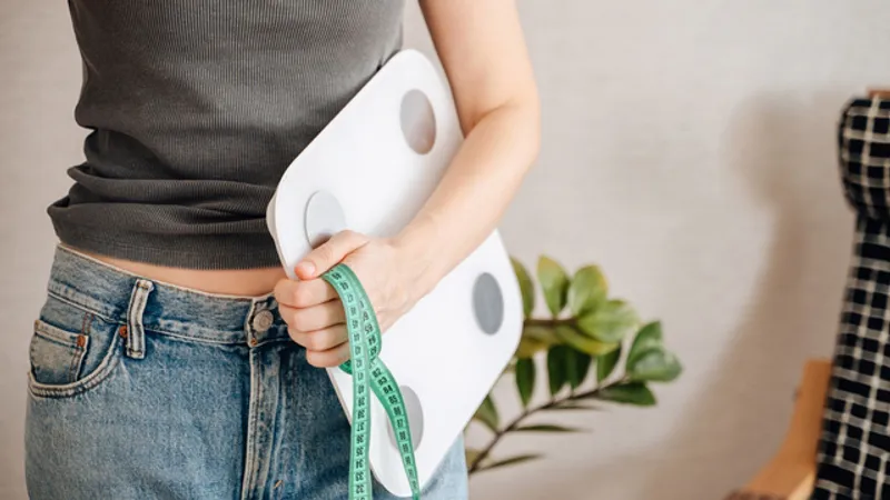 Woman holding a body scale and measuring tape.