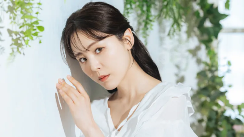 Woman in a white blouse posing beside a wall with greenery.