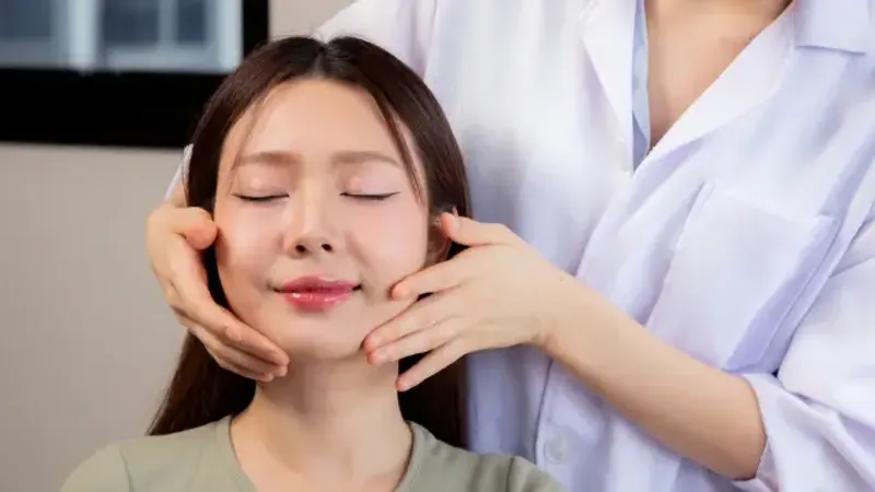 Practitioner examining a woman’s jawline with both hands.