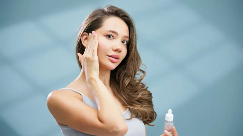 Woman applying skincare serum to her cheek while holding a dropper bottle.