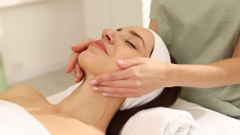 Practitioner massaging a woman’s jaw and neck during a facial treatment.