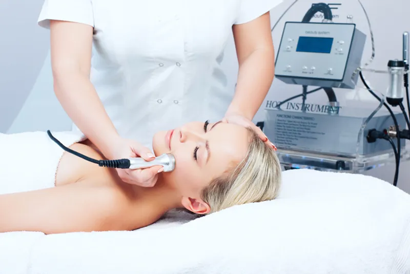 Practitioner using a handheld device on a reclining woman’s face.