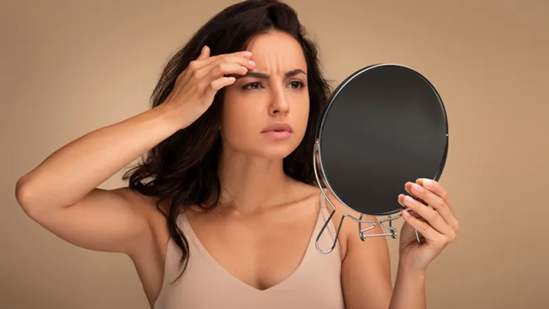 Woman looking at her eyebrow in a mirror with concern about brow sagging.