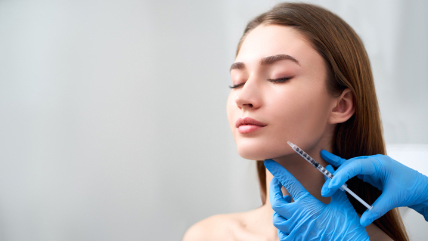 Practitioner holding a syringe near a woman’s chin, with contour lines indicating the treatment area.