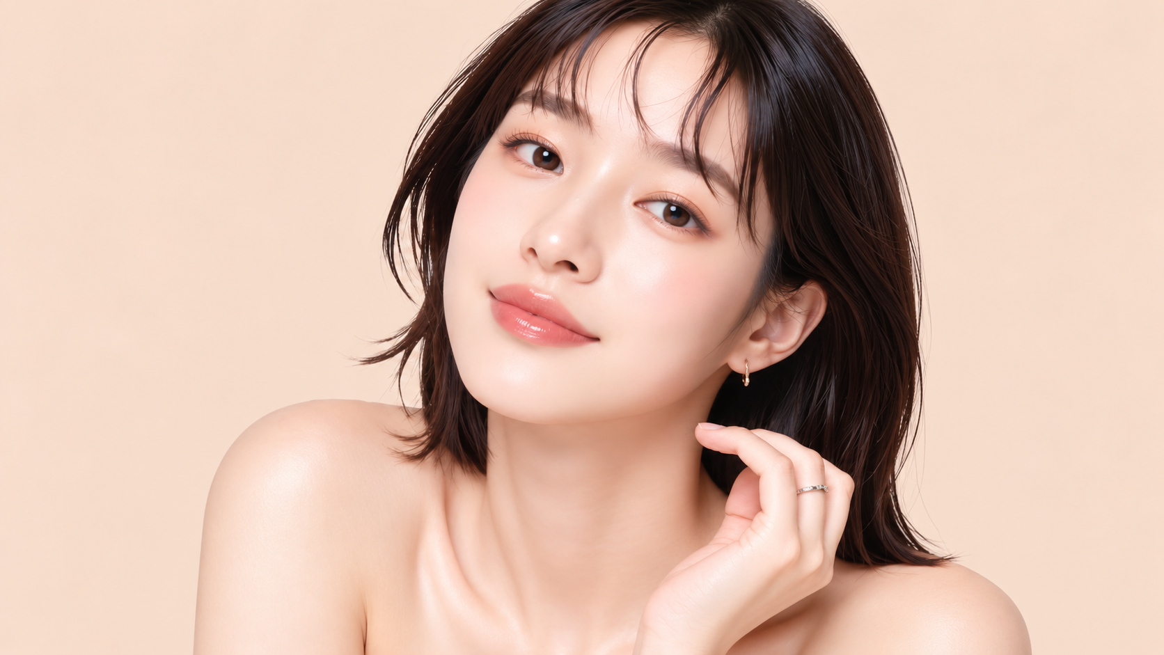 Woman with shoulder-length dark hair gently touching her jawline against a soft peach background.