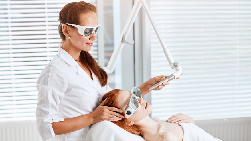 Practitioner holding a laser treatment device near a reclining woman wearing protective eyewear.