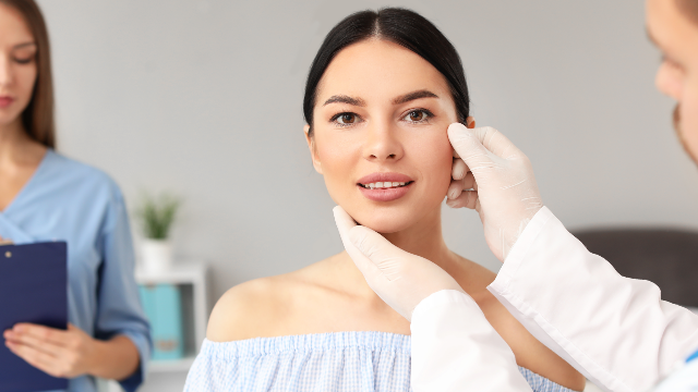 Doctor examining a patient’s face during a pre-operative assessment before facial plastic surgery.