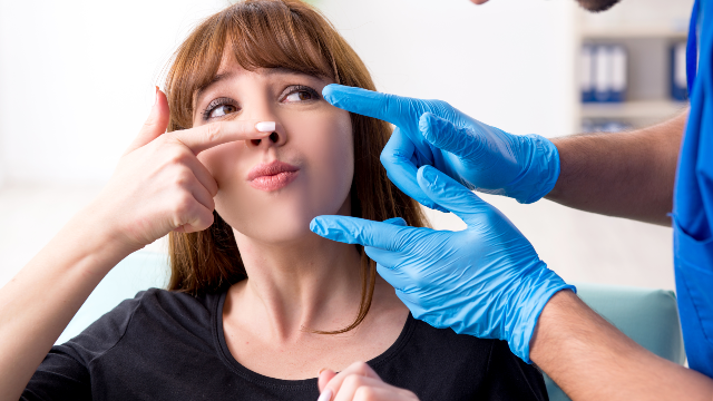 Doctor examining a patient’s nose and facial features before rhinoplasty surgery.