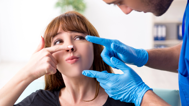 Revision rhinoplasty consultation: a surgeon closely examines a patient's nose to assess the results of a previous operation