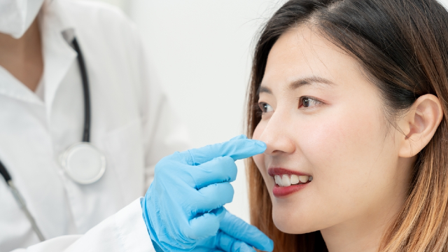 Doctor examining a patient's nasal bridge during a non-implant rhinoplasty consultation