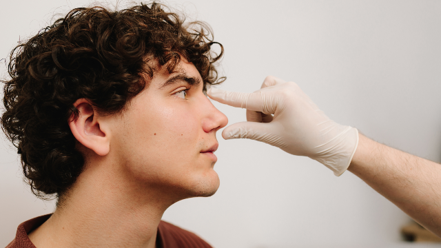 Doctor examining a patient’s nose before rhinoplasty treatment.