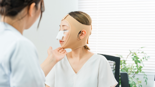 Patient recovering from rhinoplasty with nasal bandage and facial compression garment during post-op checkup
