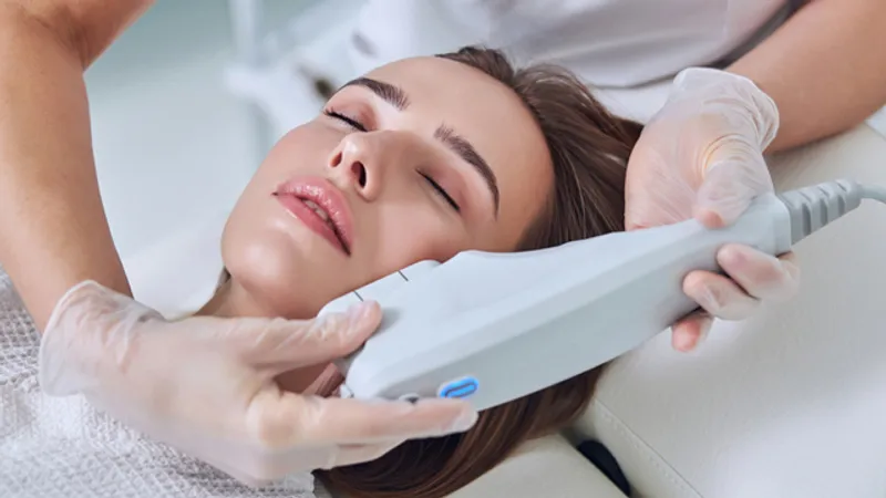 Practitioner applying a handheld treatment device to a woman’s jawline.