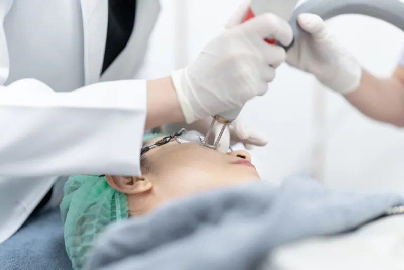 Practitioner using a handheld laser device on a woman’s face.