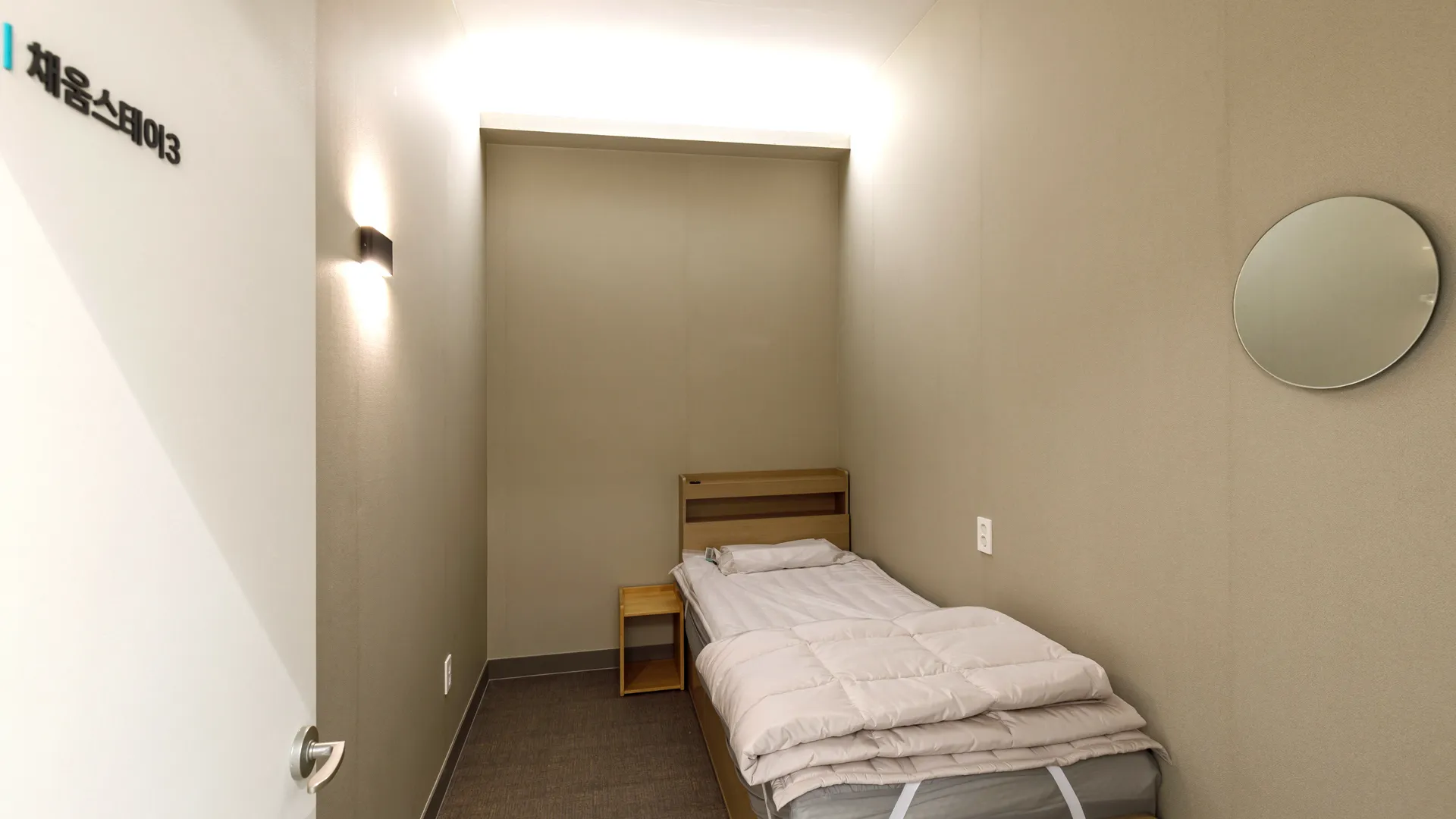 Treatment room at Seoulhoho Hospital with a single bed, bedside table, and round wall mirror.